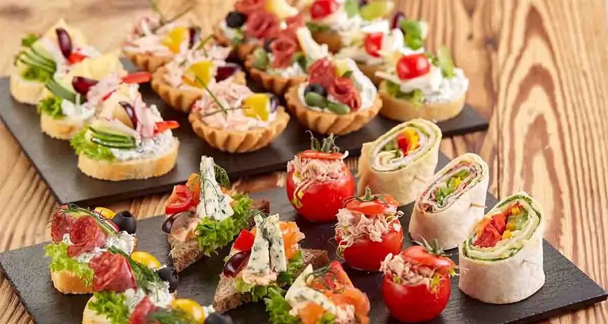 Varietà di tartine, involtini e pomodorini ripieni, perfette per idee aperitivo economico e gustoso.