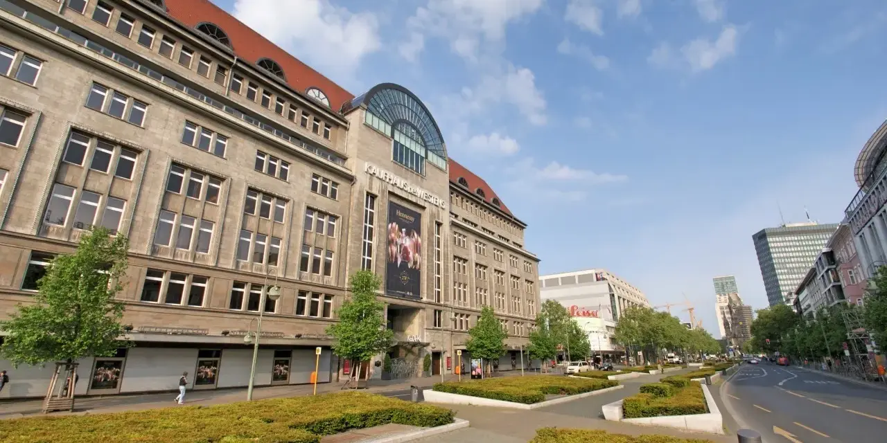 Das KaDeWe Berlin, ein imposantes Gebäude mit vielen Fenstern, steht unter einem blauen Himmel mit Wolken.