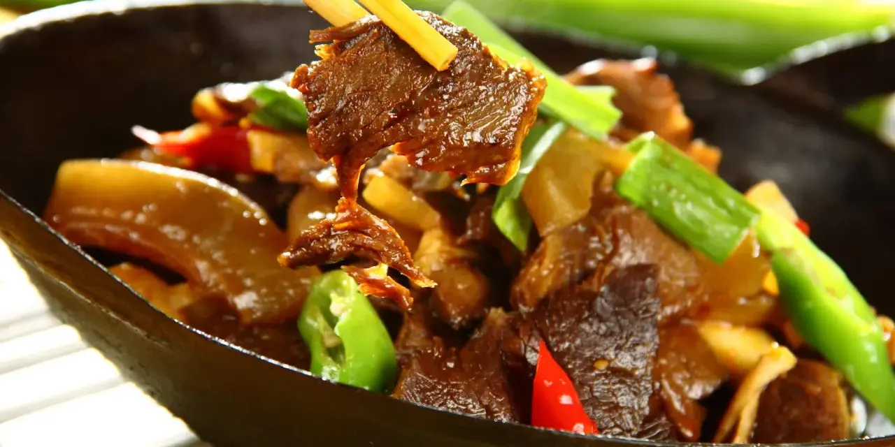 Chopsticks podnoszą kawałek aromatycznej wołowiny po chińsku z miski pełnej pysznego dania z warzywami.