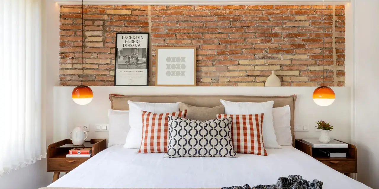 Ideas para decorar la pared de la cabecera de la cama: ladrillo visto, cuadros y lámparas naranjas.