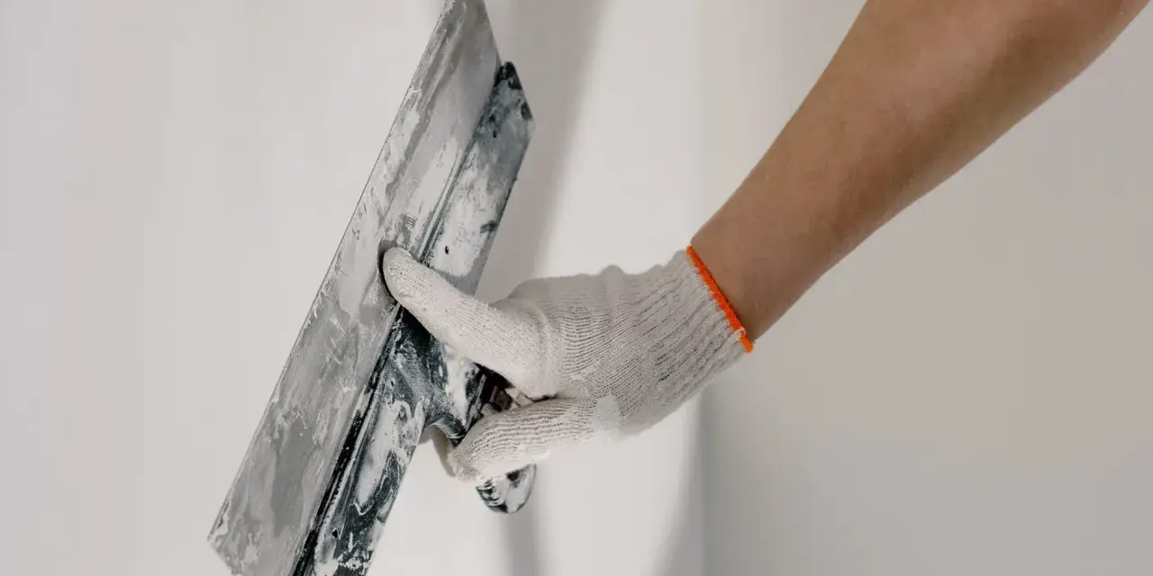 Mano enguantada alisando masilla para tapar agujeros en la pared.
