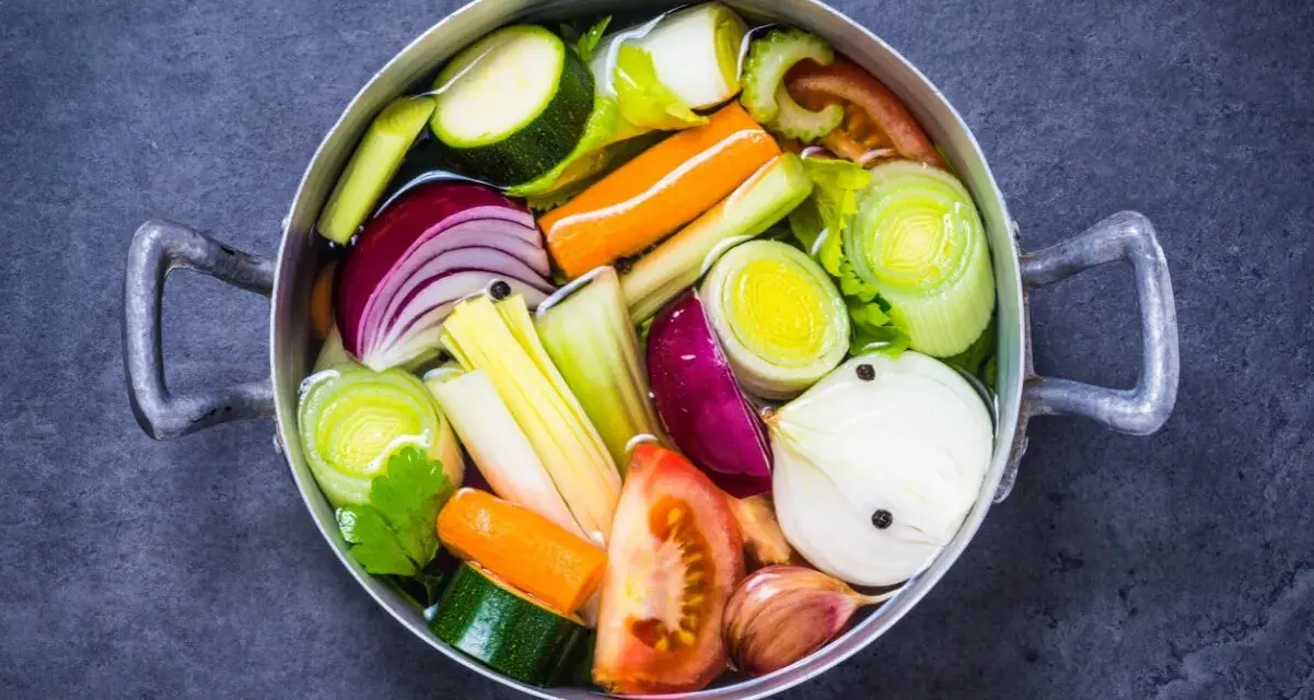 Olla con verduras cortadas en trozos: cebolla, zanahoria, calabacín, puerro, tomate y ajo.