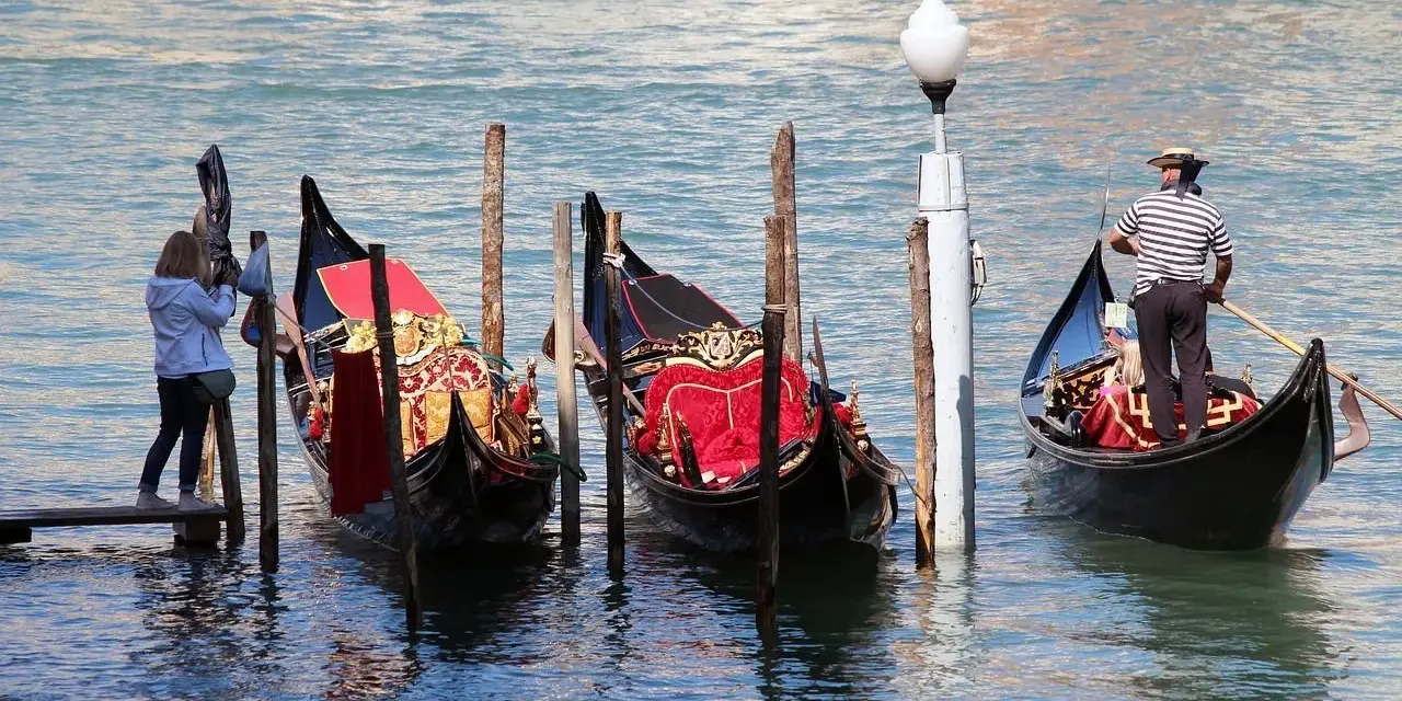 Gondole veneziane ornate, una turista scatta foto. La differenza tra gondola e sandalo è chiara: una naviga, l'altro si indossa.