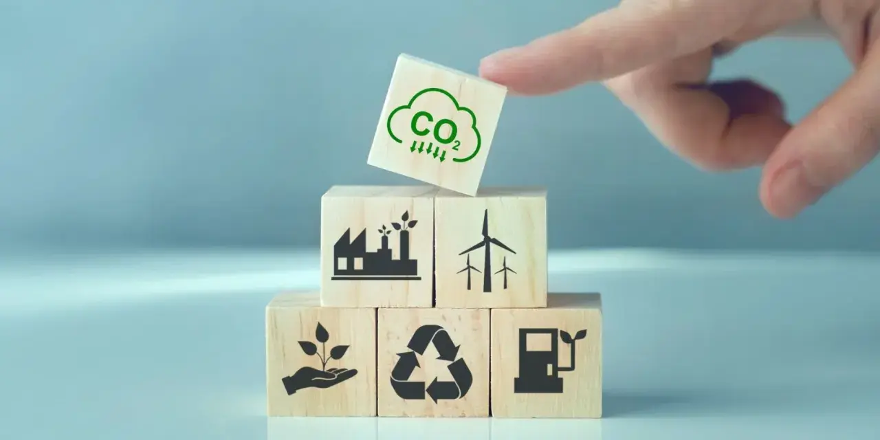 Klocki symbolizujące zielony ład: fabryka, wiatraki, sadzonka, recykling, paliwo. Na górze kostka z chmurką CO2 i strzałkami w dół.