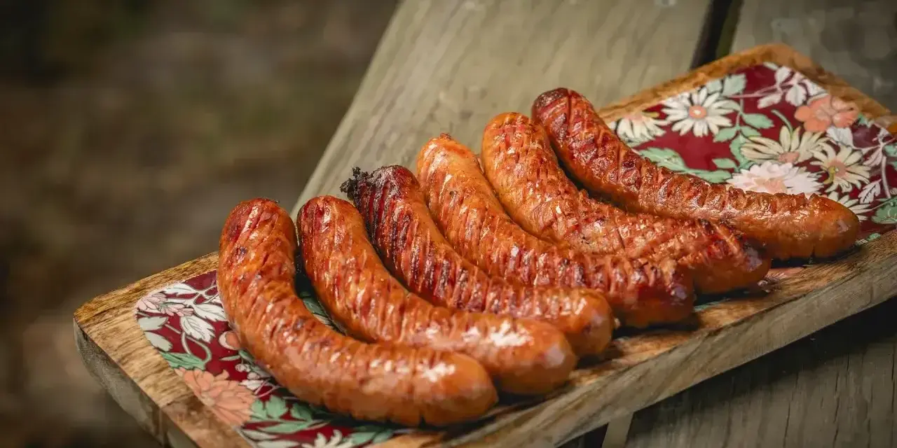 Apetyczna kiełbasa z grilla, rumiana i soczysta, ułożona na drewnianej desce z kolorowym wzorem.