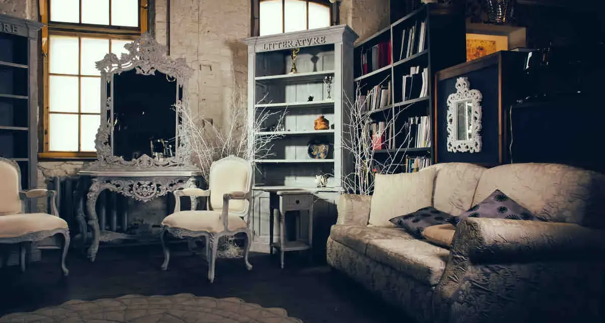 Salotto con divano, poltrone, specchio barocco e librerie. Un esempio di arredamento massimalista che unisce elementi classici e decorazioni elaborate.