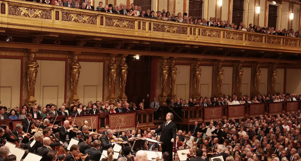 Un director dirige una orquesta sinfónica ante un público entusiasta, interpretando obras de Beethoven en un teatro majestuoso.