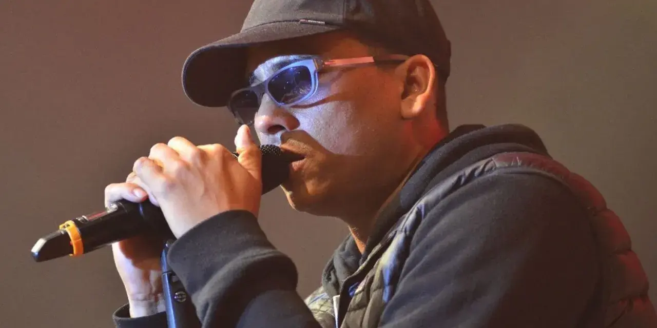 Mann mit Kappe und Sonnenbrille singt ins Mikrofon. Ein starker musik comeback Moment.