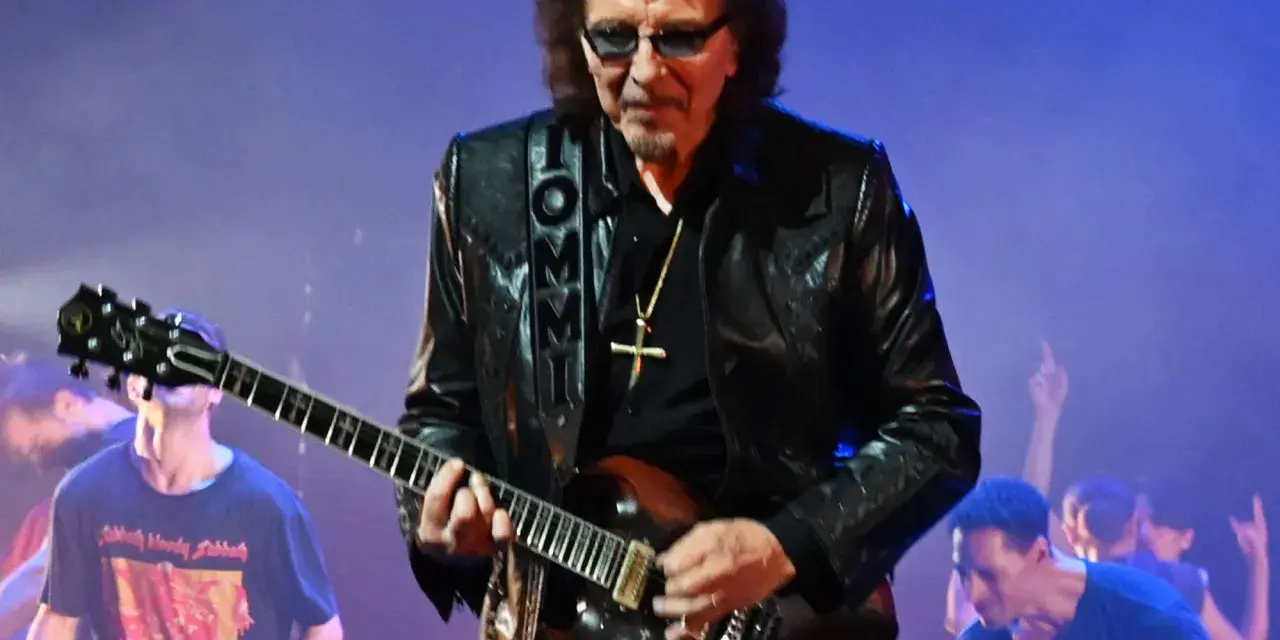Tony Iommi, Gitarrist von Black Sabbath, spielt auf der Bühne. Im Hintergrund jubelt das Publikum.