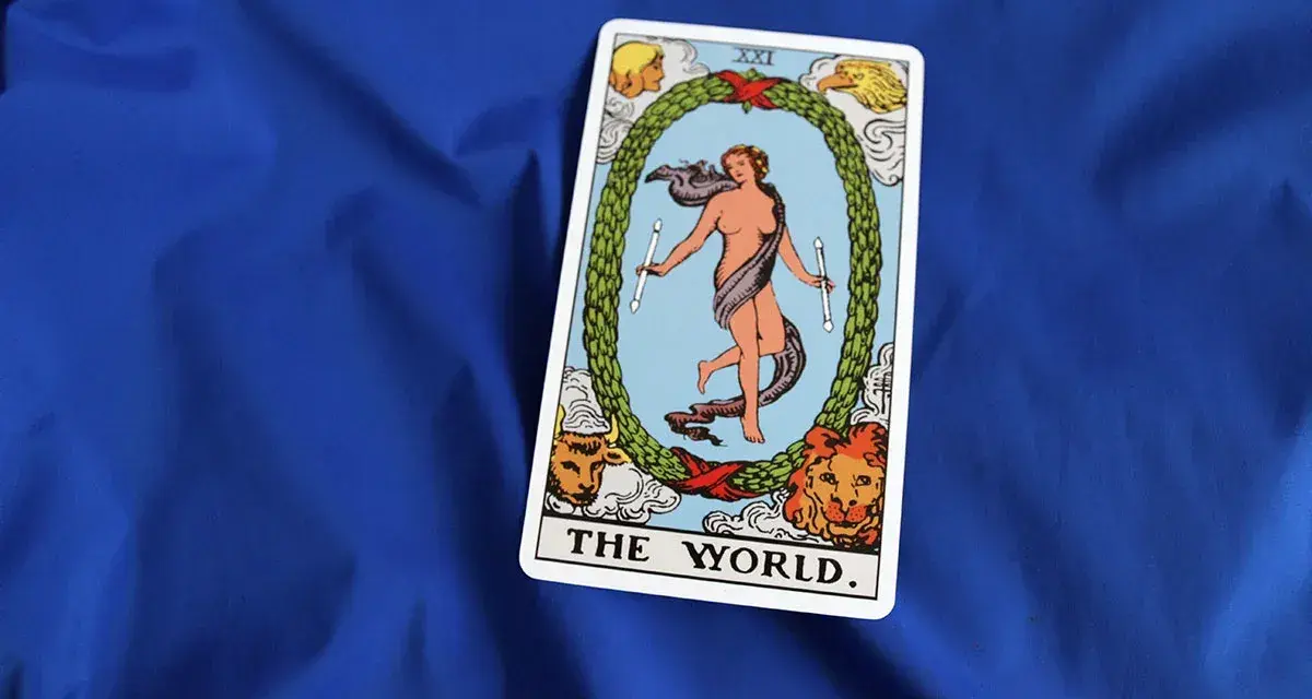 Karta "The World" z talii tarota, symbolizująca zakończenie cyklu i spełnienie, leży na niebieskim tle.