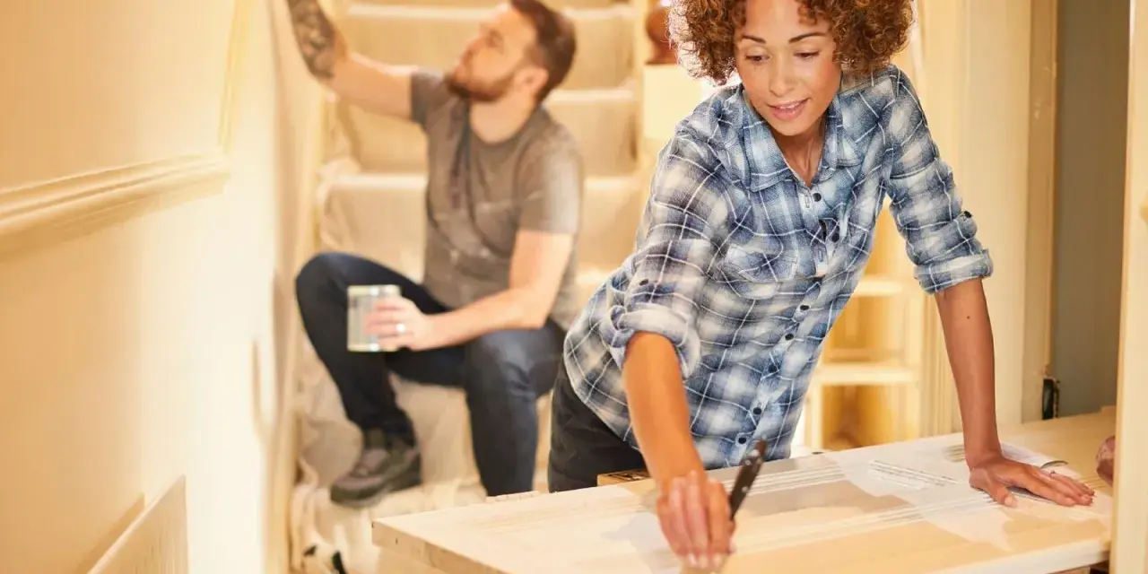 Pareja renovando su hogar con una reforma sin obras. Ella pinta una puerta, él la pared.