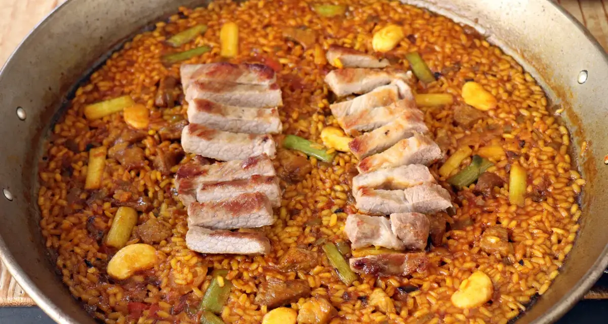 Arroz con secreto, un plato de paella con cerdo tierno y verduras crujientes, listo para ser disfrutado.
