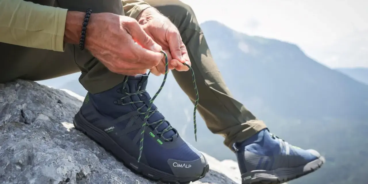 Uomo lega i lacci di scarponi da hiking su roccia, pronto per il trekking in montagna.