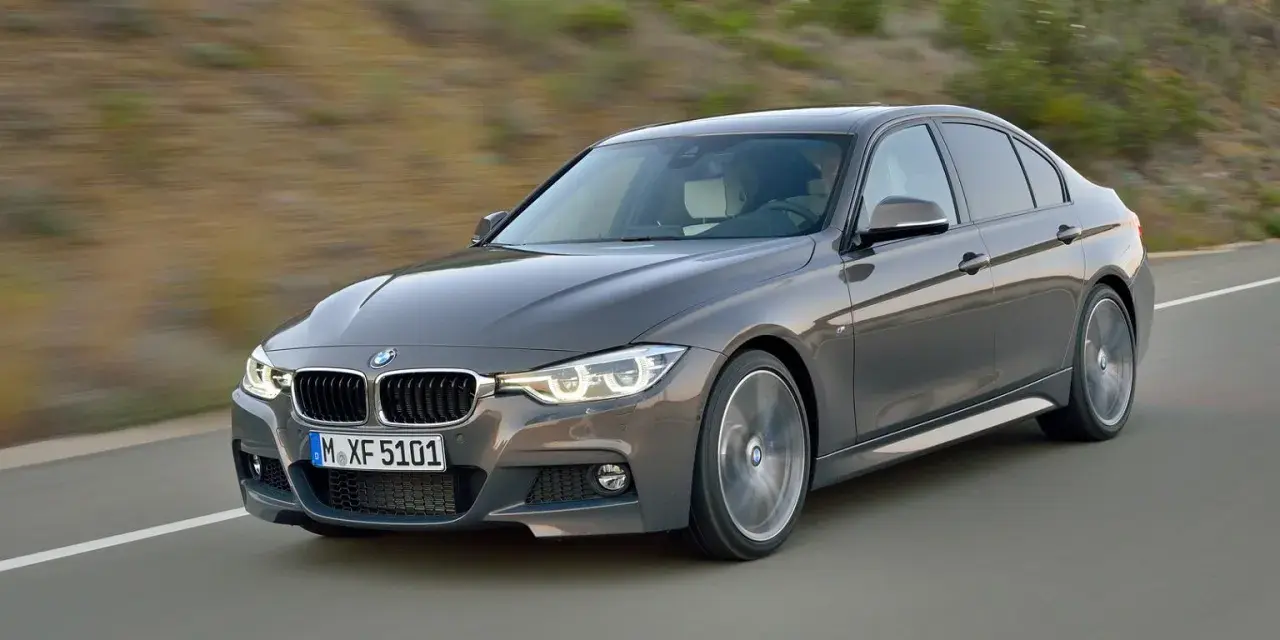 Szary sedan BMW F30 z dynamicznymi silnikami pędzi po drodze, ukazując sportowy charakter.