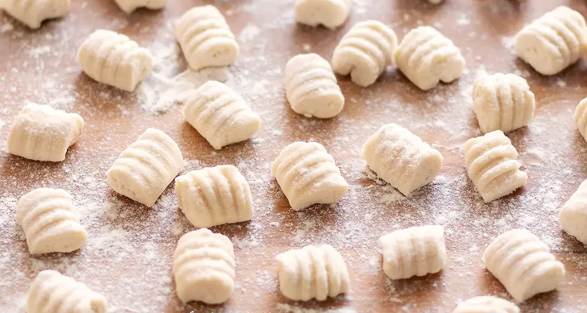 Gnocchi di ricotta freschi, pronti per essere cucinati, spolverati di farina su un tagliere di legno.