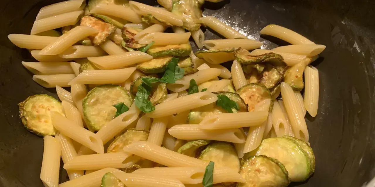 Penne con zucchine saltate e basilico fresco, un classico piatto di pasta e zucchine alla siciliana, pronto per essere gustato.
