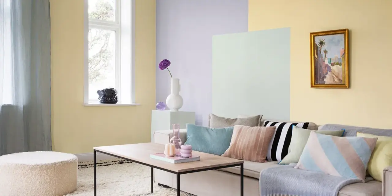 Ett vardagsrum med pastell inredning. Ljusgula, ljuslila och ljusgröna väggar skapar en mjuk atmosfär. En beigefärgad soffa är fylld med kuddar i olika pastellfärger och mönster.