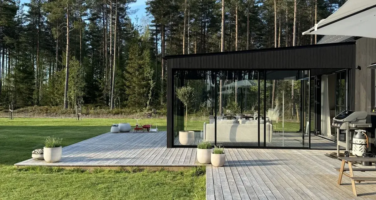 Modernt uterum med glaspartier och träaltan, perfekt för att bygga ett drömhem vid skogen.