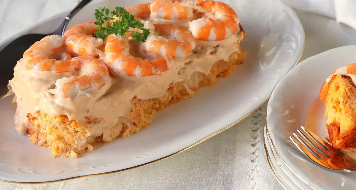 Delicioso pudin de pescado cubierto con crema y camarones, decorado con perejil.