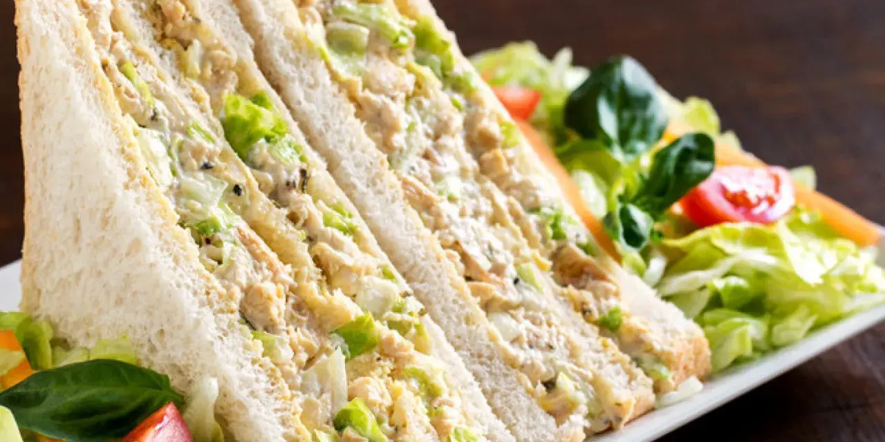 Sándwich de pollo cortado en triángulos, relleno de pollo desmenuzado y lechuga, acompañado de ensalada fresca.