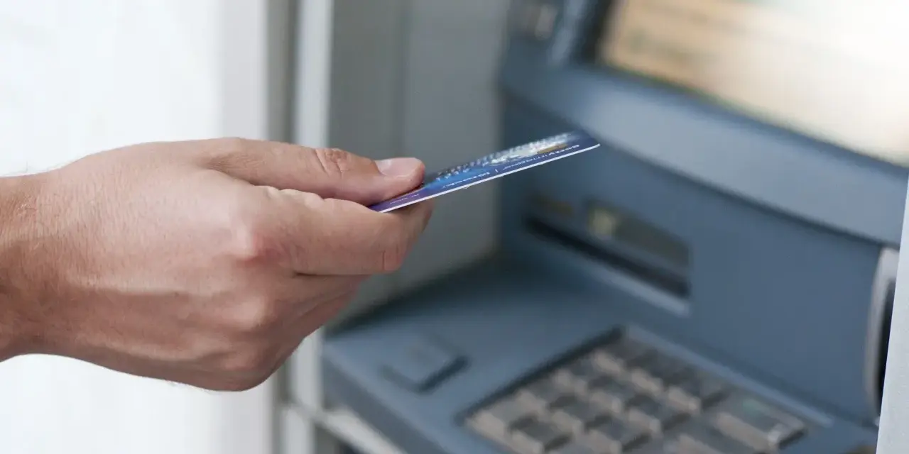 Dłoń z kartą zbliża się do bankomatu. Może to być związane z obsługą konta w Credit Agricole, a nie z zajęciami komorniczymi.