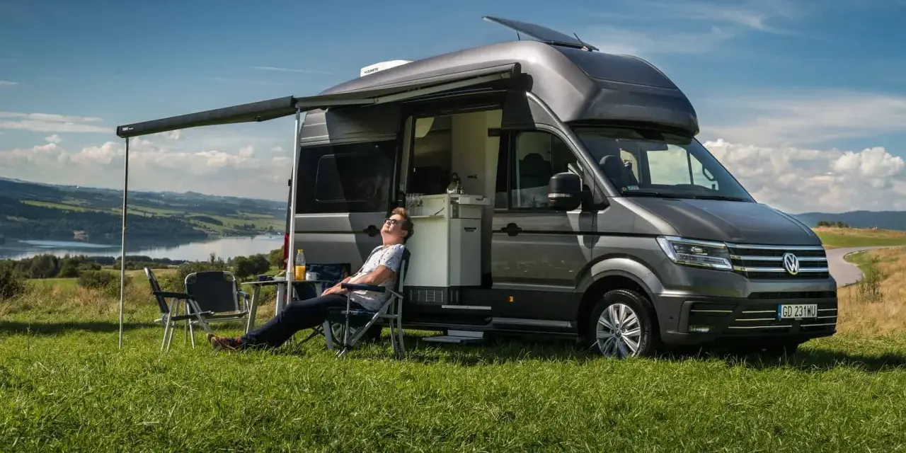 Mężczyzna odpoczywa przy kamperze VW California. Wymiary tego pojazdu pozwalają na komfortowe podróżowanie i biwakowanie.
