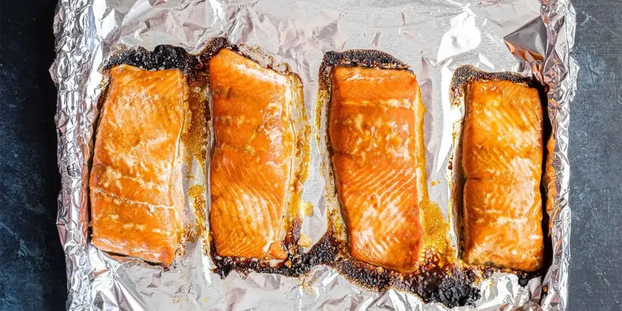 Cztery kawałki łososia pieczone na folii aluminiowej, gotowe do przygotowania sushi.