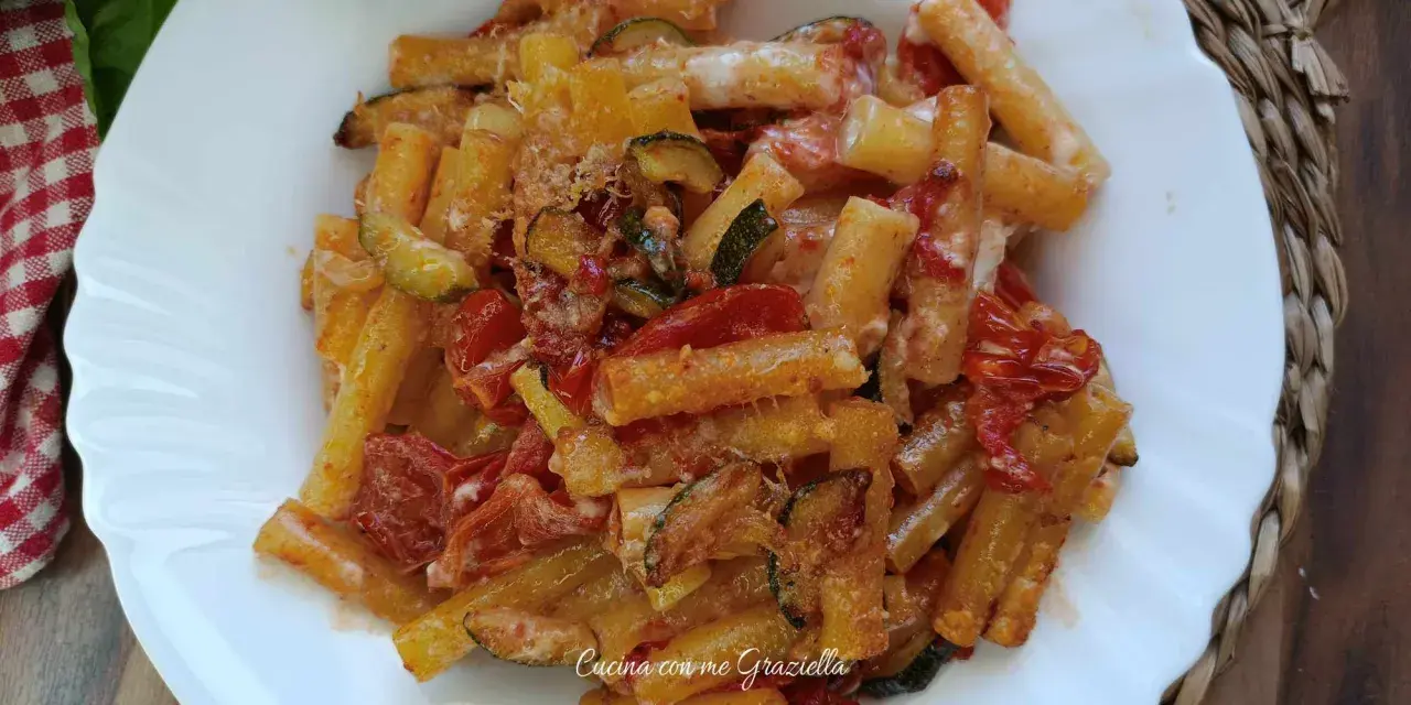 Piatto di pasta con zucchine e pomodorini, condita con formaggio grattugiato e basilico fresco.