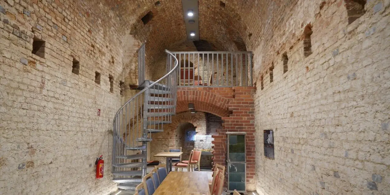 Wnętrze restauracji Srebrna Góra z kamiennymi ścianami, kręconymi schodami i drewnianymi stołami.