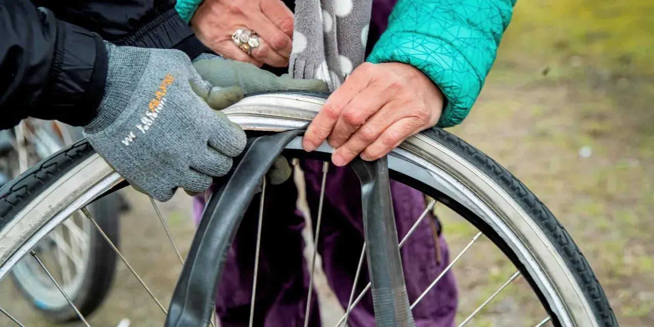 Två personer byter cykelslang. En med grå handske och en med grön jacka och prickig scarf.
