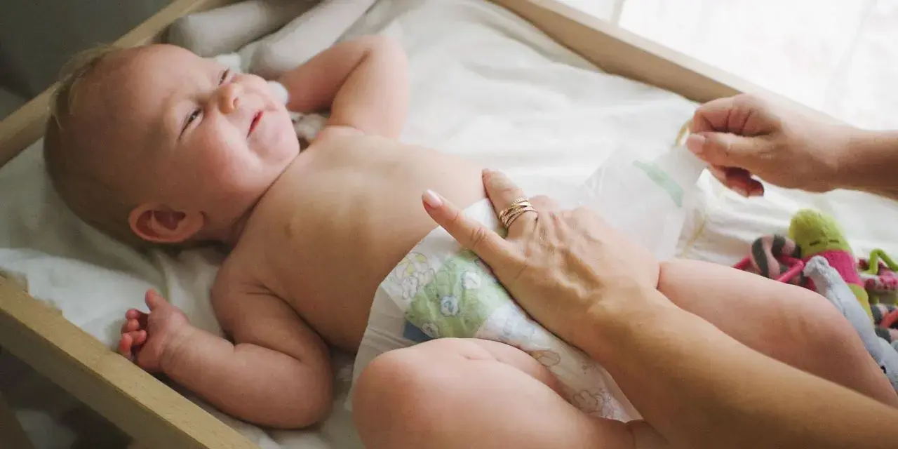 Radość noworodka podczas pielęgnacji. Mama zmienia pieluszkę, maluch uśmiecha się, leżąc na przewijaku wśród zabawek.