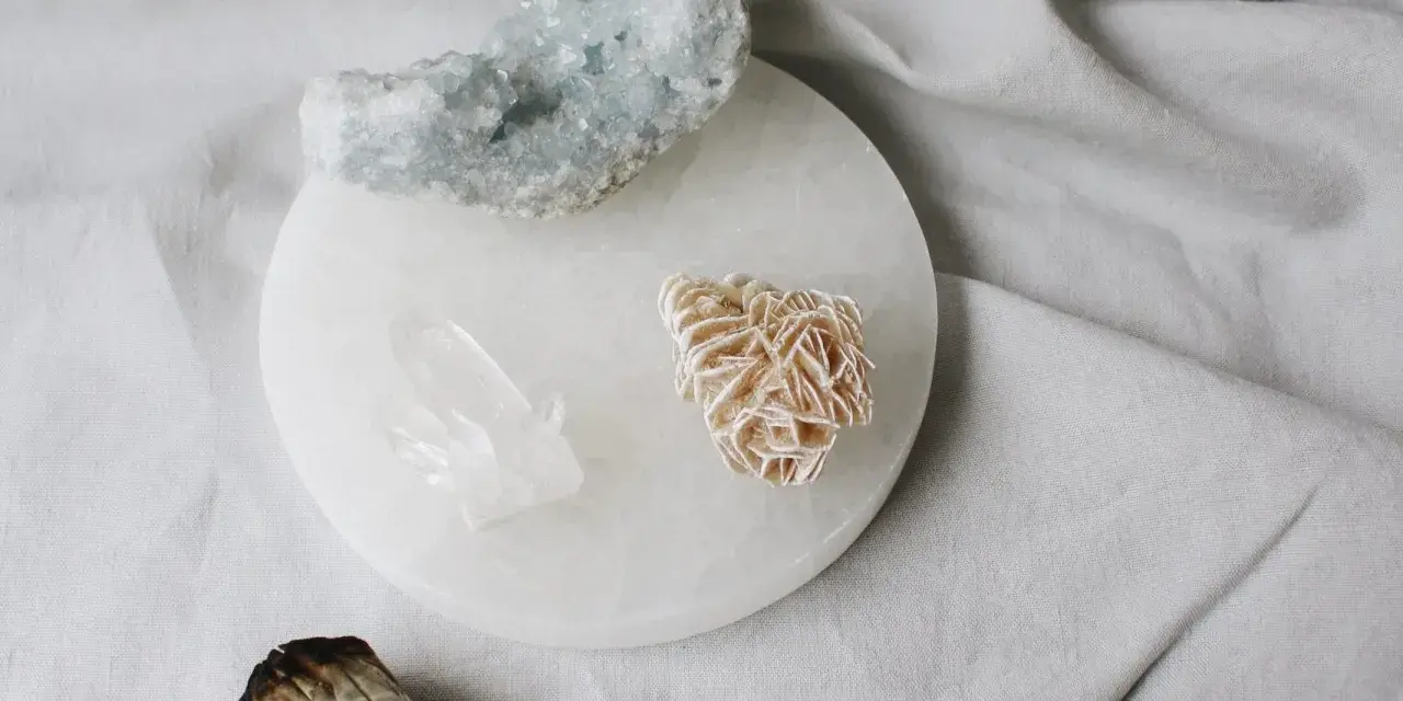 Cristales de selenita, cuarzo y amatista sobre un plato de selenita, junto a un manojo de salvia. Guía para saber como limpiar la selenita.