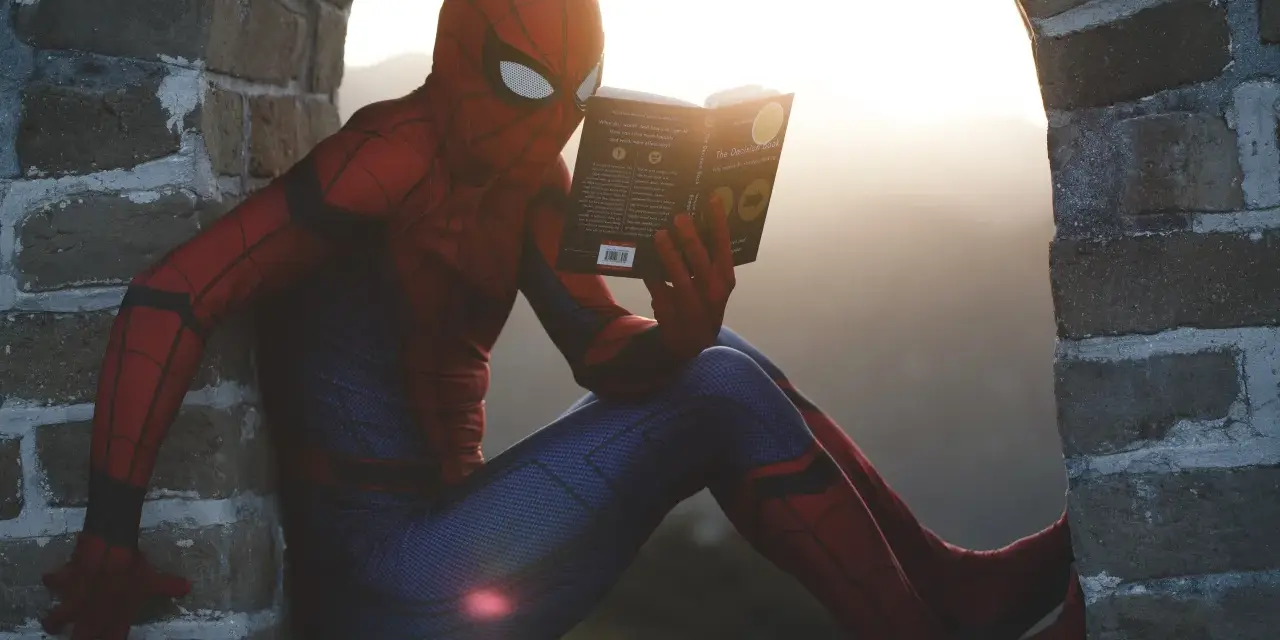 Spider-Man w czerwonym stroju siedzi na murze i czyta książkę. Czy komiks to utwór literacki? Nawet superbohaterowie potrzebują chwili wytchnienia i wiedzy.