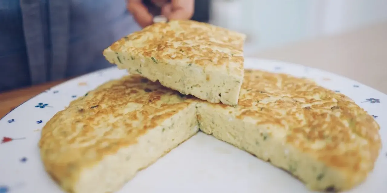 Una fetta di frittata, preparata con la ricetta perfetta, viene sollevata da un piatto decorato.