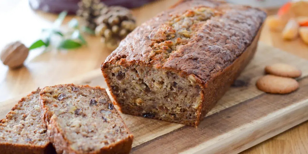 Un délicieux cake banane, coupé en tranches, sur une planche en bois. Des noix et des biscuits complètent cette gourmandise.