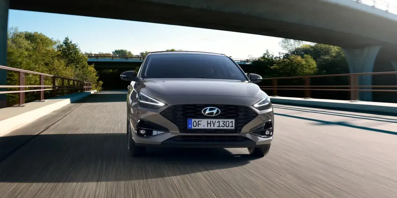 Szary Hyundai i30 1.4 benzyna pędzi po drodze pod mostem, otoczony zielenią.