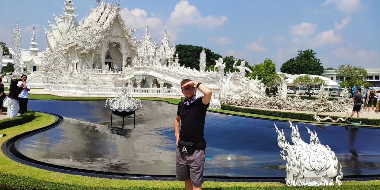 Mężczyzna pozuje przed olśniewającą białą świątynią Wat Rong Khun w Chiang Rai.