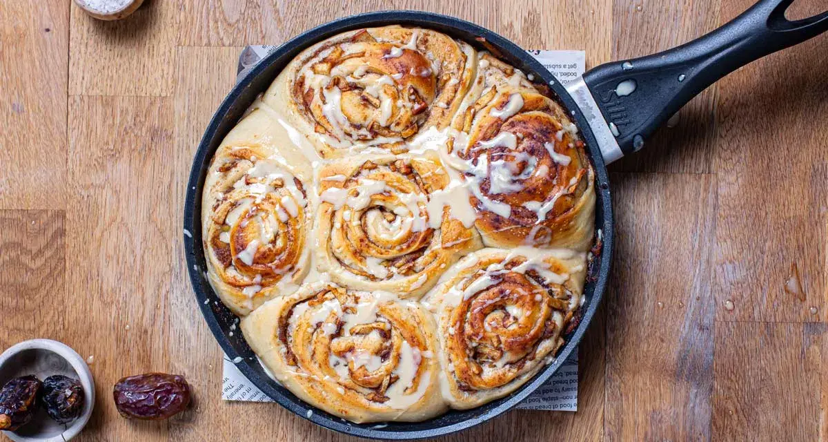 Frisch gebackene Zimtschnecken mit Apfelstückchen und Zuckerguss in einer Pfanne. Ein köstliches Apfel Zimtschnecken Rezept zum Nachbacken.