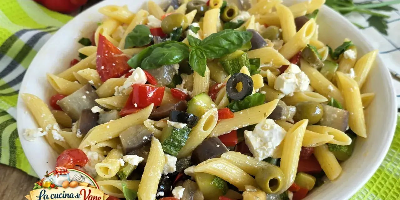 Pasta fredda con feta, peperoni, zucchine, melanzane e olive nere. Un piatto estivo colorato e saporito.