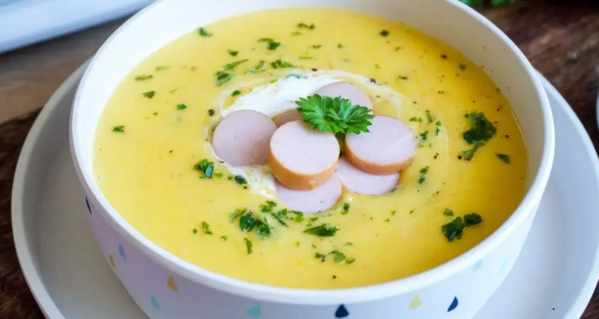 Cremige Kartoffelsuppe, zubereitet im Thermomix, garniert mit Würstchenscheiben, einem Klecks Sahne und Petersilie.