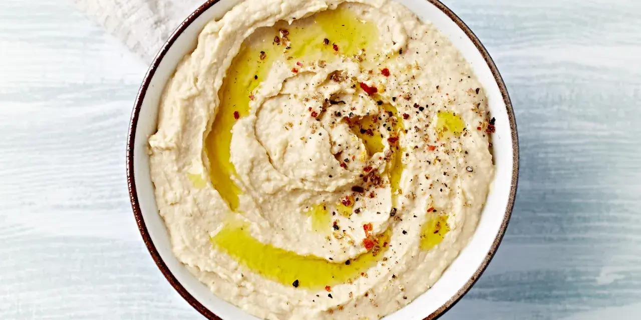Kremowy, gładki hummus polany oliwą i posypany przyprawami. Idealny do maczania pieczywa.