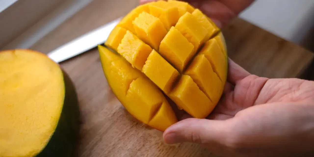 Hände halten ein perfekt geschnittenes Mango-Viertel, bereit zum Genießen. Das Fruchtfleisch ist in Würfel geschnitten, was das Mango schneiden erleichtert.