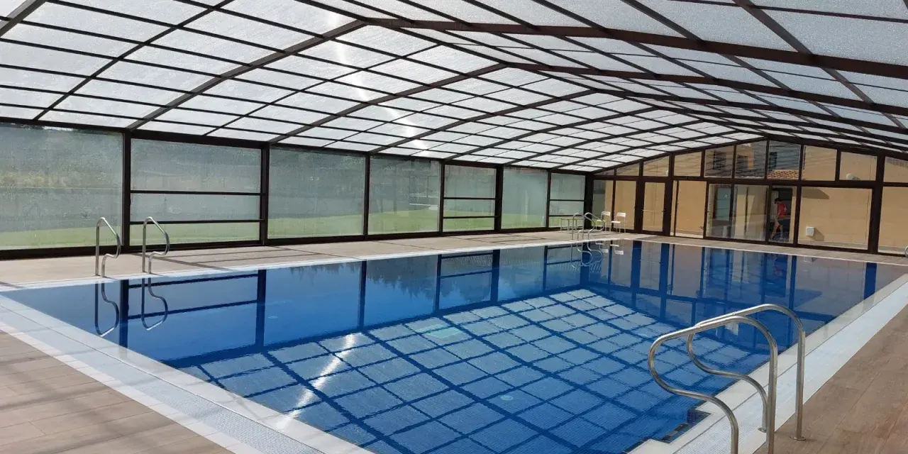 Una piscina cubierta con techo transparente y paredes de cristal, ideal para disfrutar todo el año. Estos porches para piscinas ofrecen un espacio acogedor.