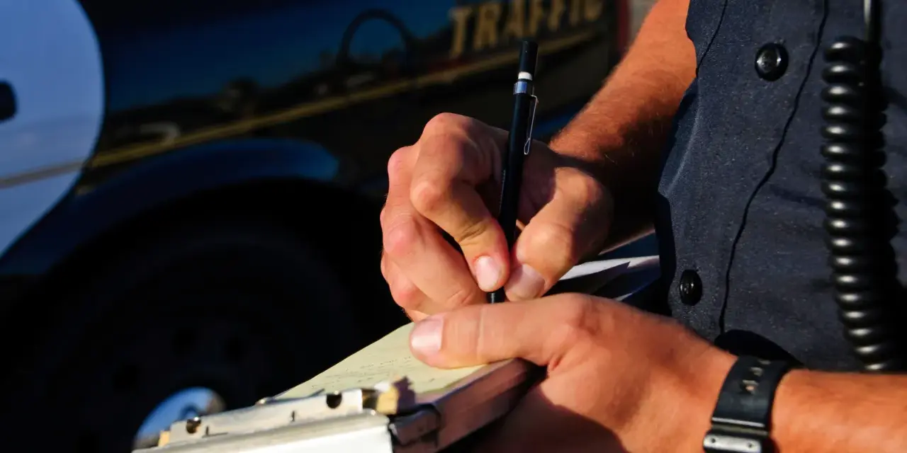 Agente di polizia scrive una multa, forse per infrazione all'art. 71 cds, vicino a un'auto della polizia.