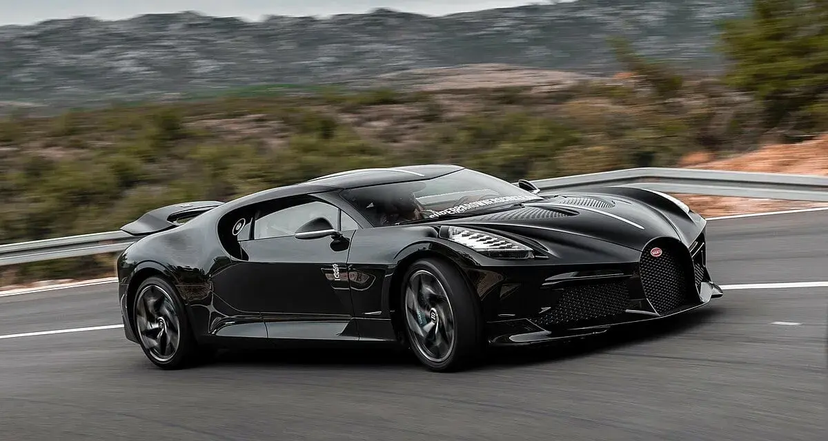 Czarny Bugatti La Voiture Noire pędzi po krętej drodze, otoczony przez górzysty krajobraz.