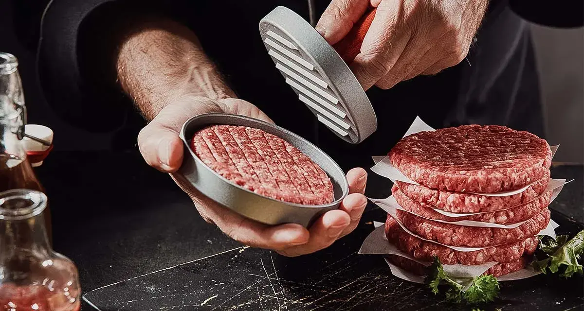 Frische burger patties werden mit einem Patty-Former geformt. Ein Stapel fertiger Patties liegt daneben.
