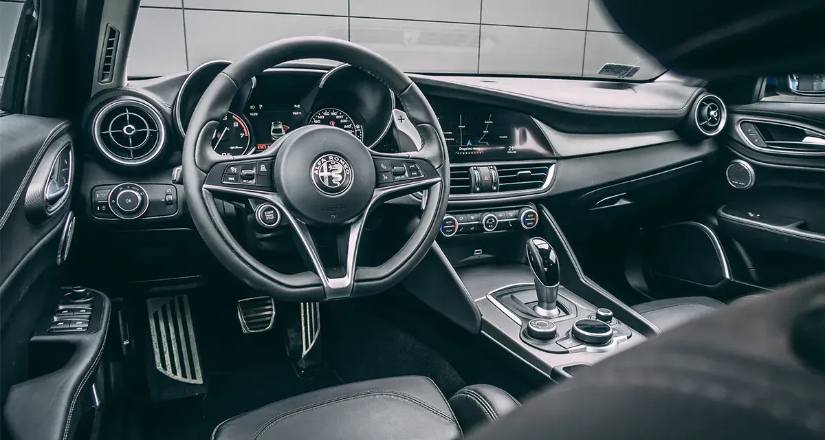 Wnętrze luksusowego samochodu Alfa Romeo. Kierownica, deska rozdzielcza i dźwignia zmiany biegów. Ta fotografia samochodowa oddaje styl i komfort.