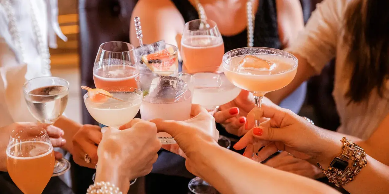 Frauen stoßen mit bunten Cocktails an. Ein fröhlicher Anlass für Day Drinking mit Freundinnen.