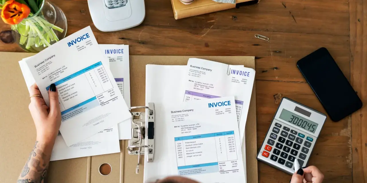 Manos revisando facturas y calculando el total. Aprende como hacer una factura a mano.