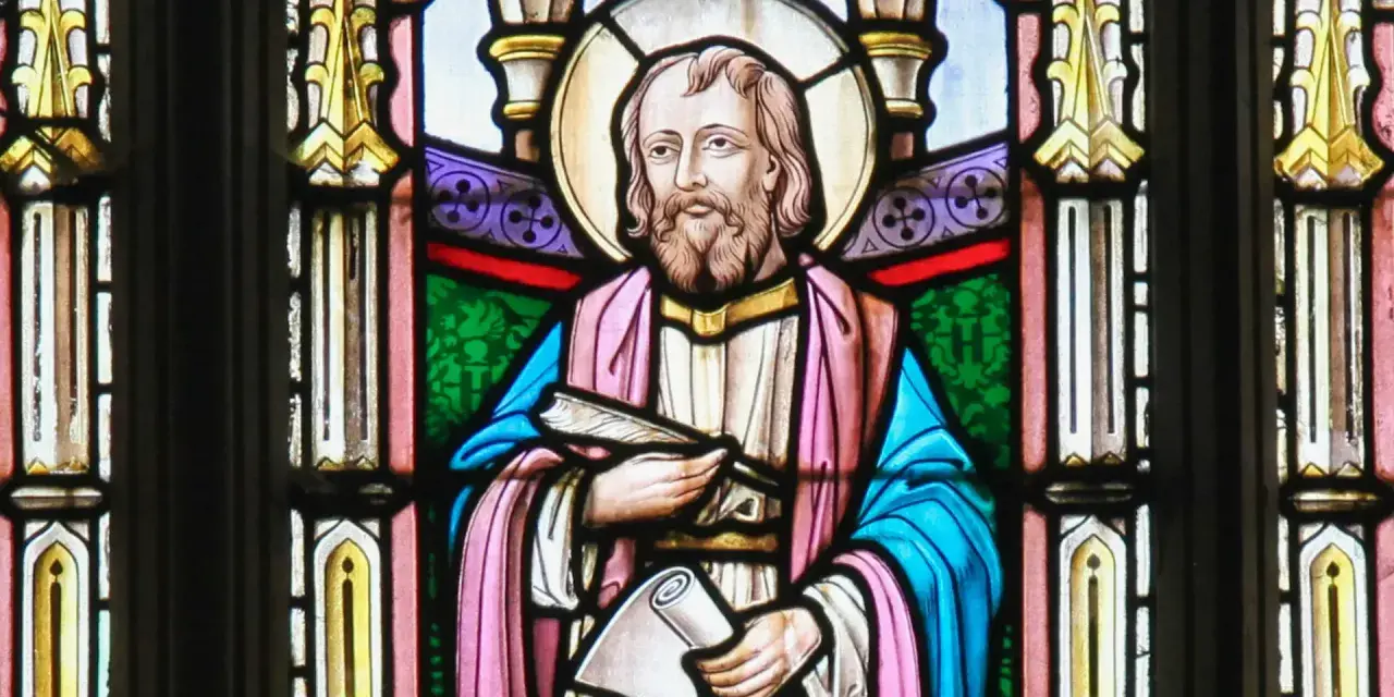 Witraż przedstawia świętego Łukasza z księgą i zwojem, symbolizując jego rolę jako ewangelisty i pisarza.
